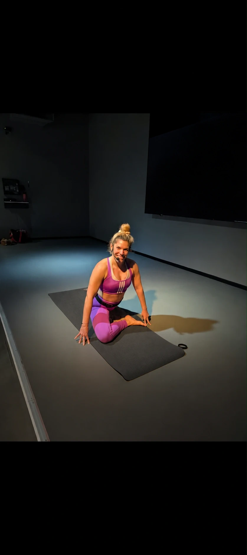 Simone sitzt in Sportkleidung auf einer Trainingsmatte im Studio